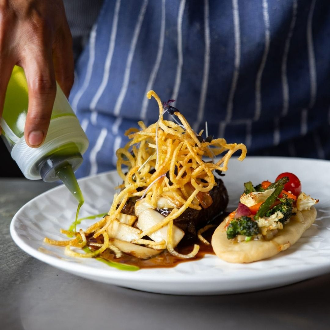 Una persona está vertiendo salsa en un plato de comida.