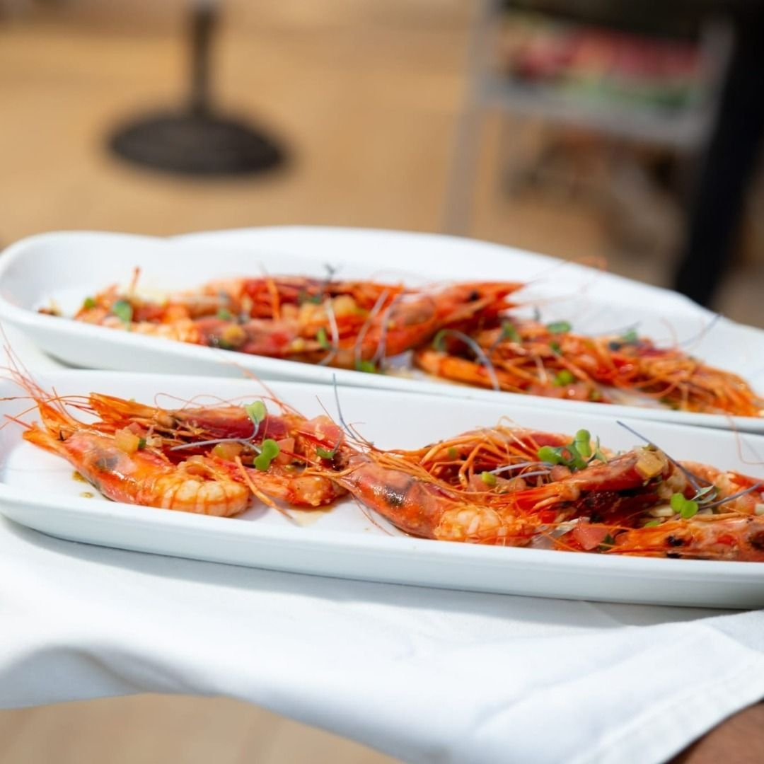 Una persona sostiene dos platos de camarones sobre un paño blanco.