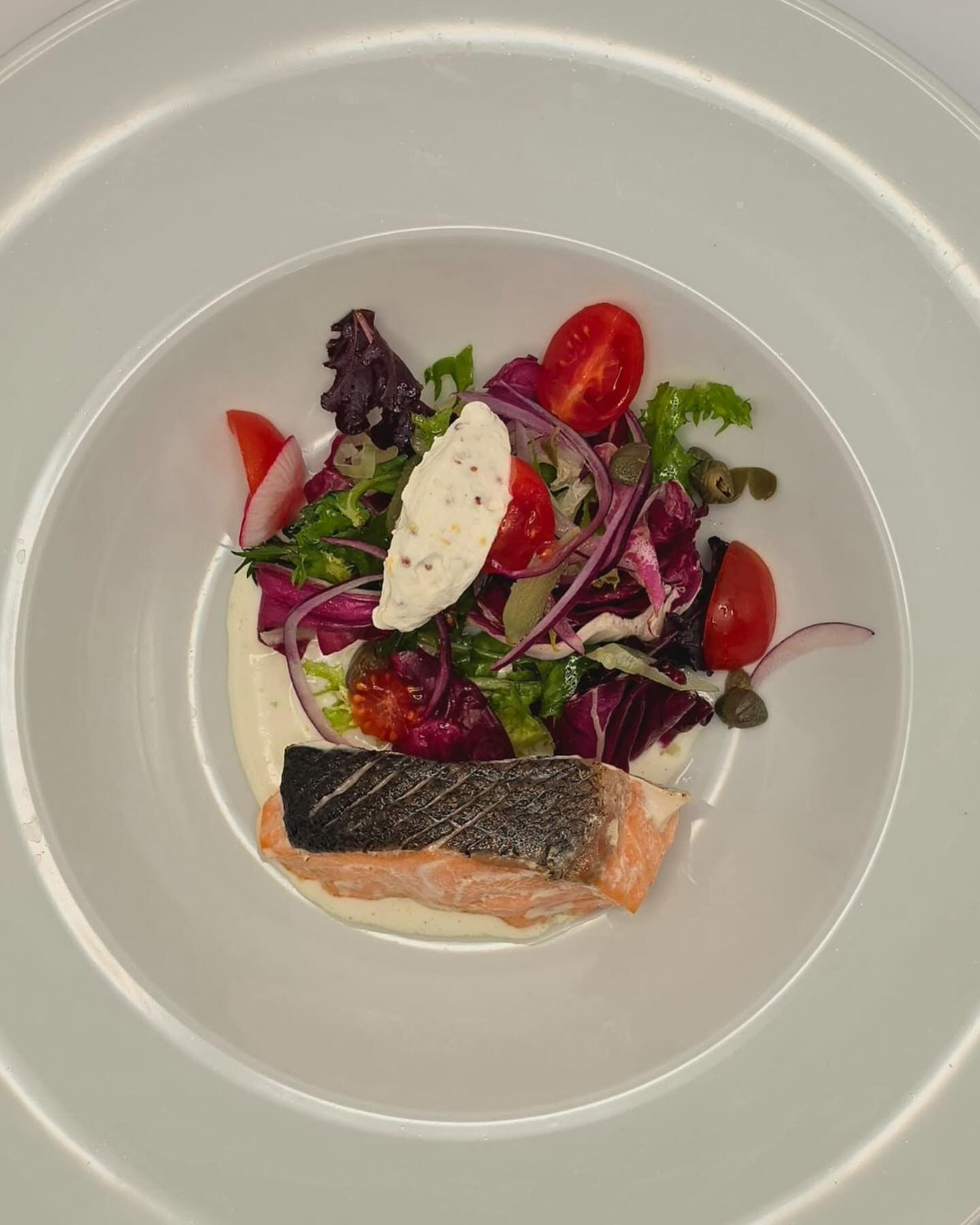 Un plato blanco cubierto con una ensalada y un trozo de salmón.