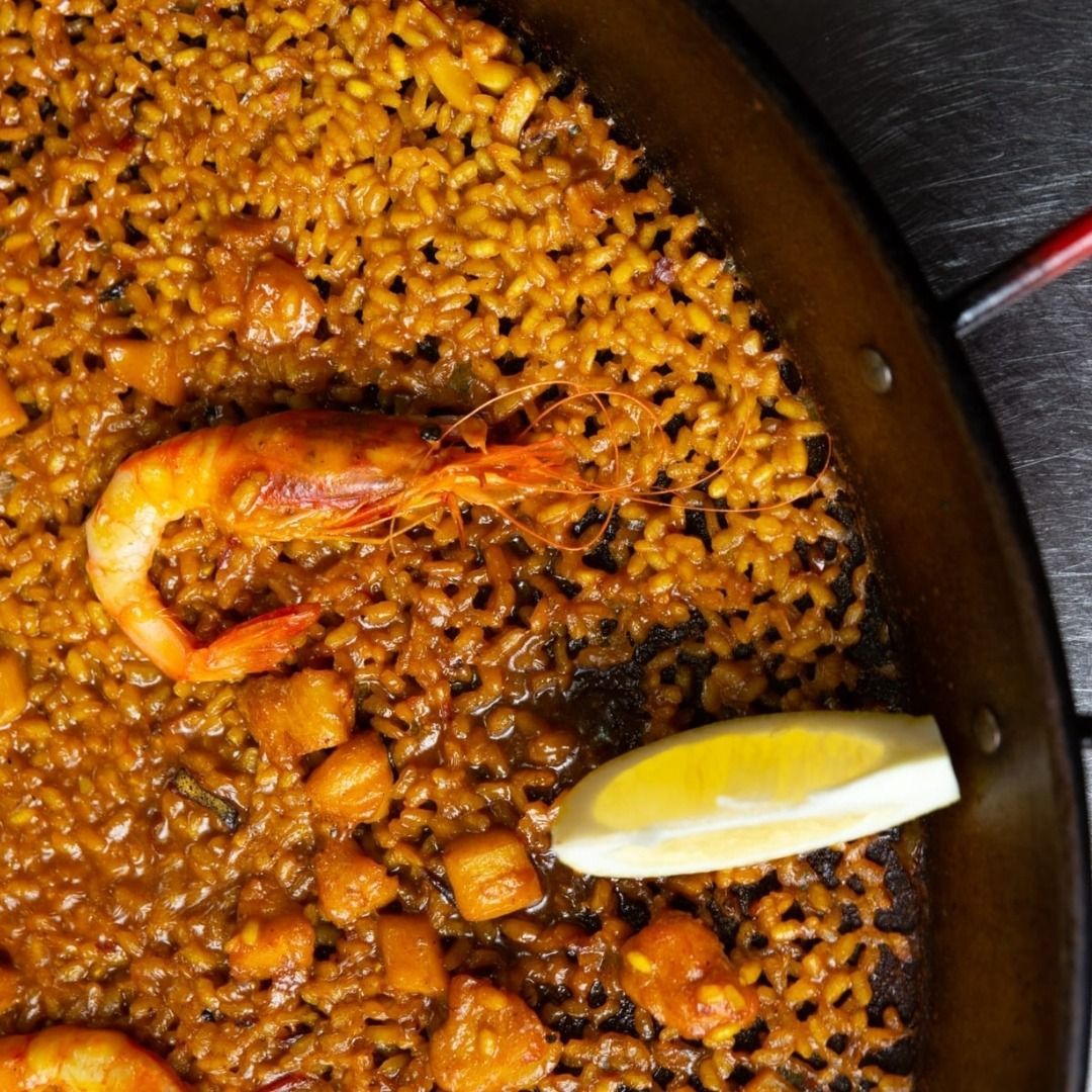 Un primer plano de una paella con camarones y una rodaja de limón.