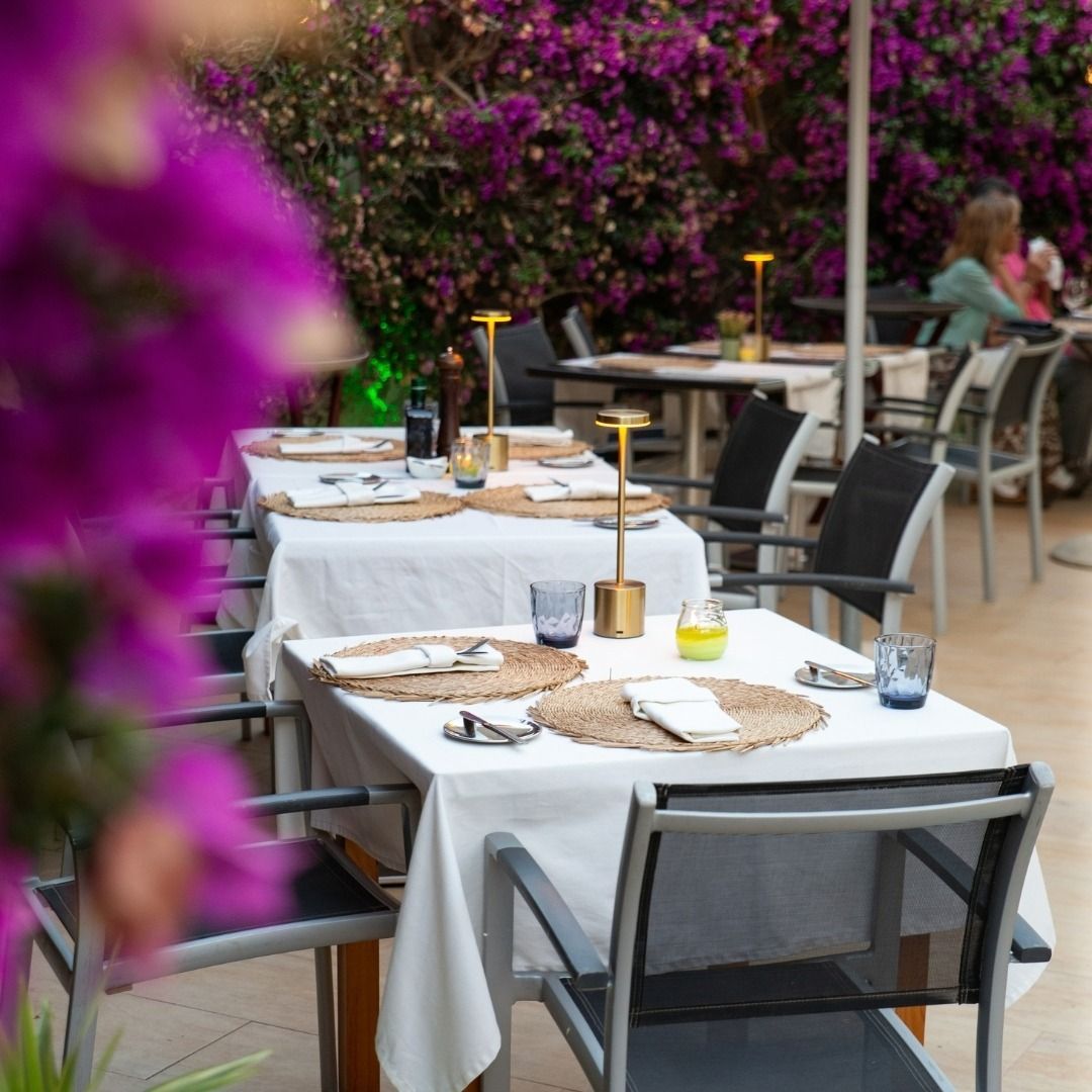 Un restaurante con mesas y sillas y flores moradas al fondo.