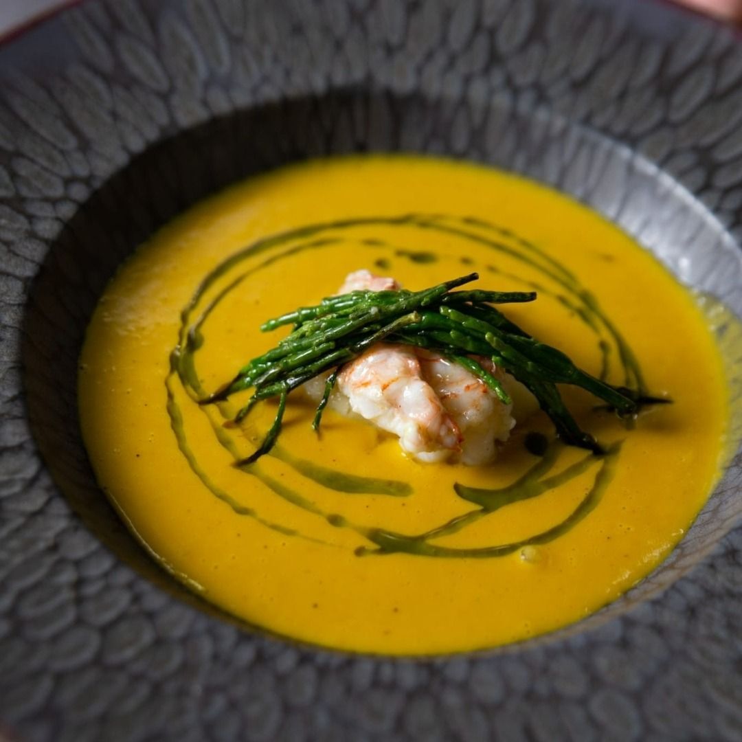 Un tazón de sopa con camarones y judías verdes encima.