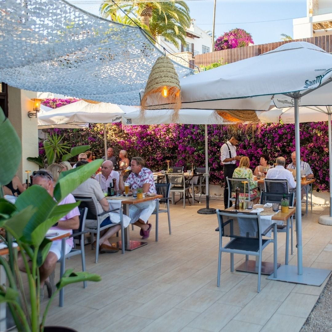 Un grupo de personas están sentadas en mesas bajo sombrillas en un restaurante.