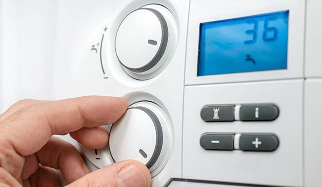 Une main tourne un bouton de thermostat blanc à côté d'un affichage numérique bleu.