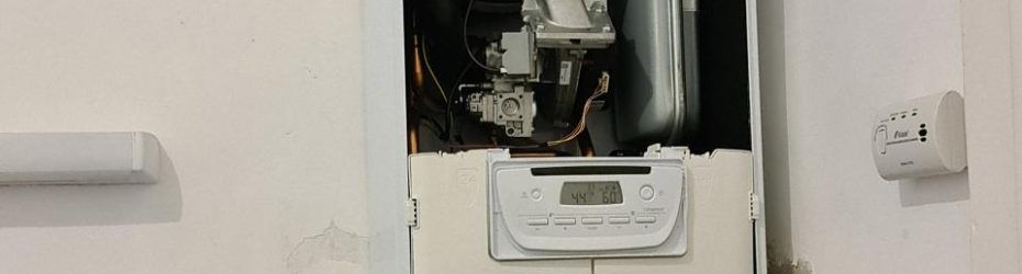 Thermostat mural et petit tableau électrique sur un mur blanc avec câblage apparent.