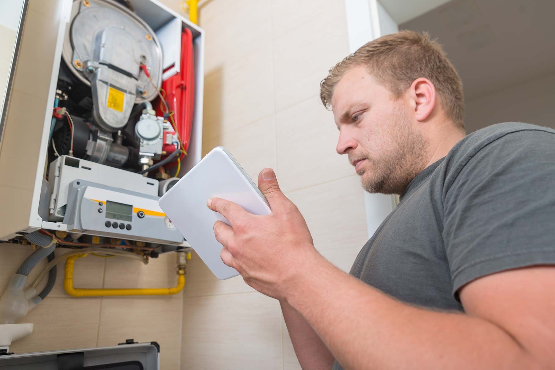 Un technicien inspecte un tableau électrique ouvert et prend des notes sur une tablette dans une salle technique.