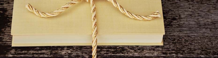Pile de livres couleur crème, attachés par une corde beige, sur une surface en bois sombre.