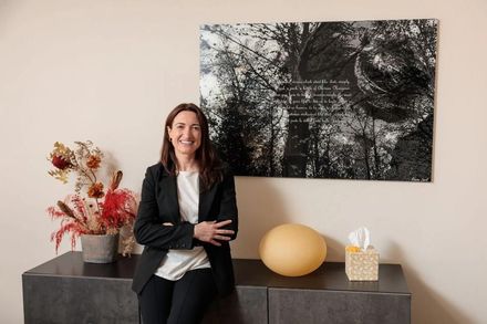 Una persona con camisa azul claro y las manos juntas está sentada junto a un médico con bata blanca.
