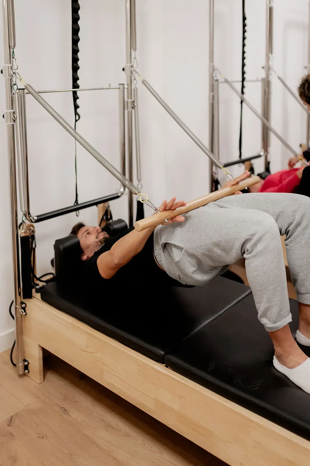 Un hombre está acostado en una máquina de pilates con un palo de madera en la mano.