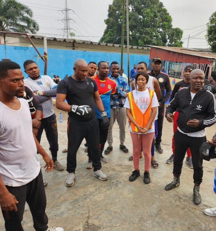 Un groupe de personnes, certaines en tenue de sport, dans un espace extérieur. Une personne portant des gants de boxe est au premier plan.