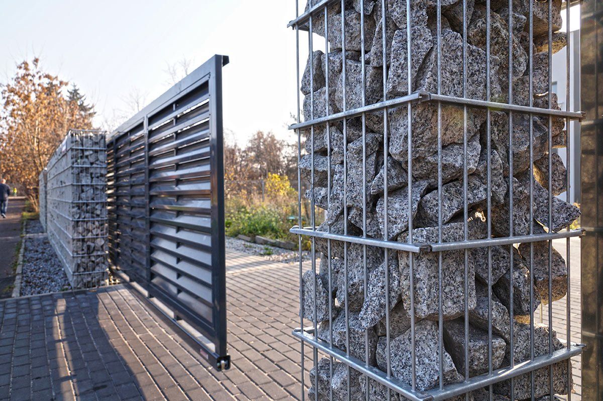 Portail d'entrée automatique utilisé en combinaison avec un mur en gabion.