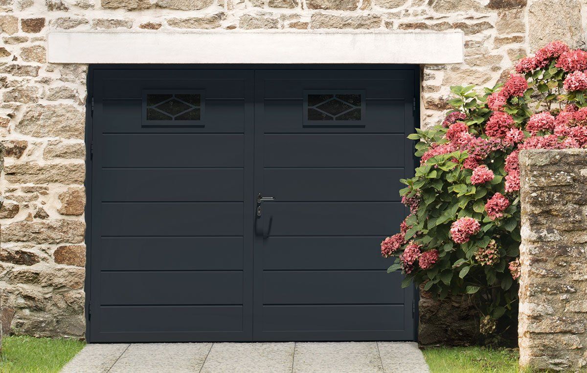 Porte de garage battante noire sur une façade en pierre