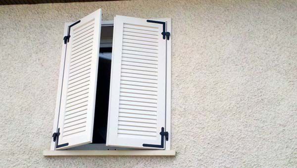 Volets battants blancs de type persienne à demi-fermés