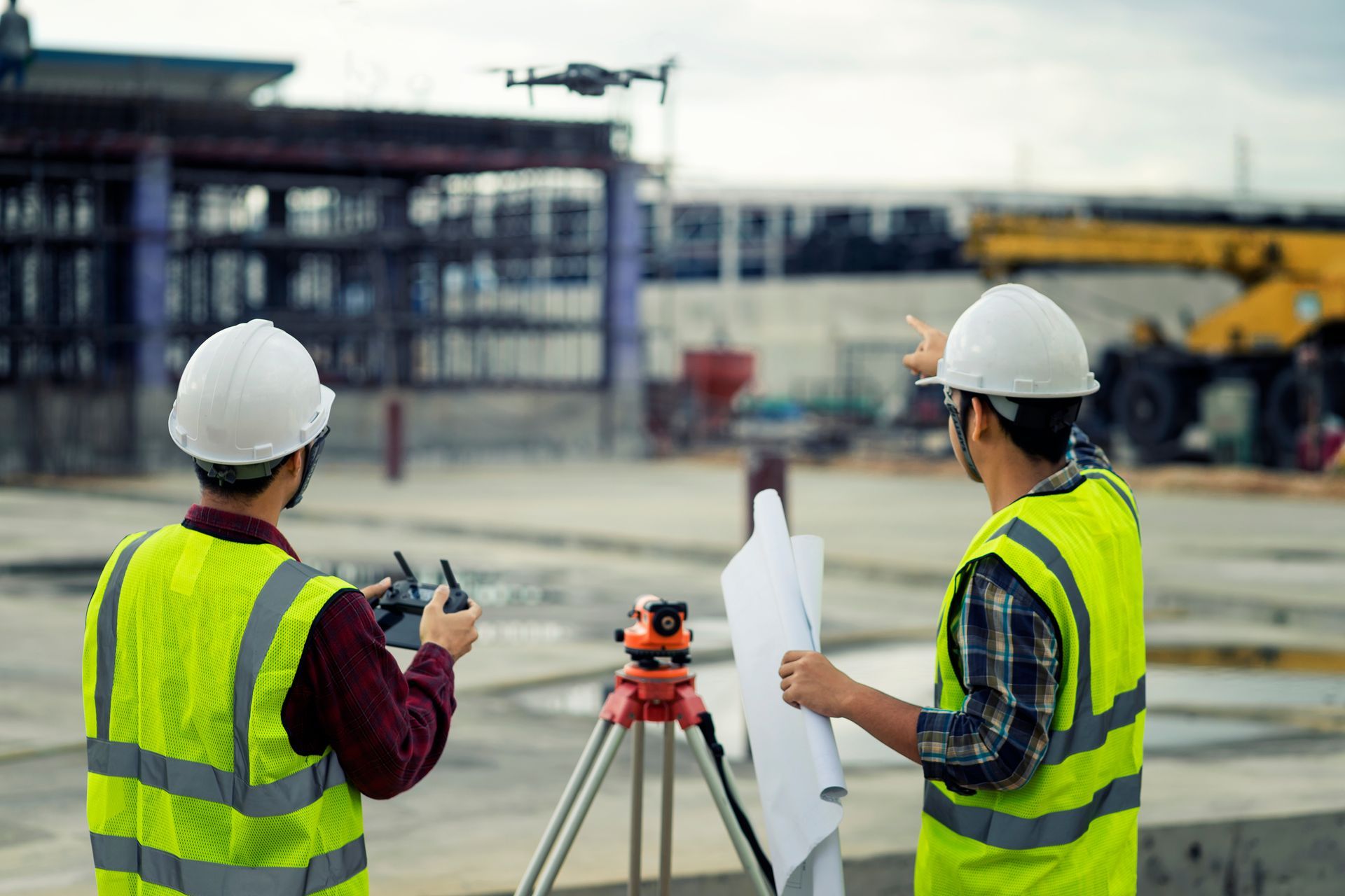 Due operai edili, con indosso giubbotti ad alta visibilità e caschi di sicurezza, manovrano un drone in un cantiere mentre esaminano i progetti.