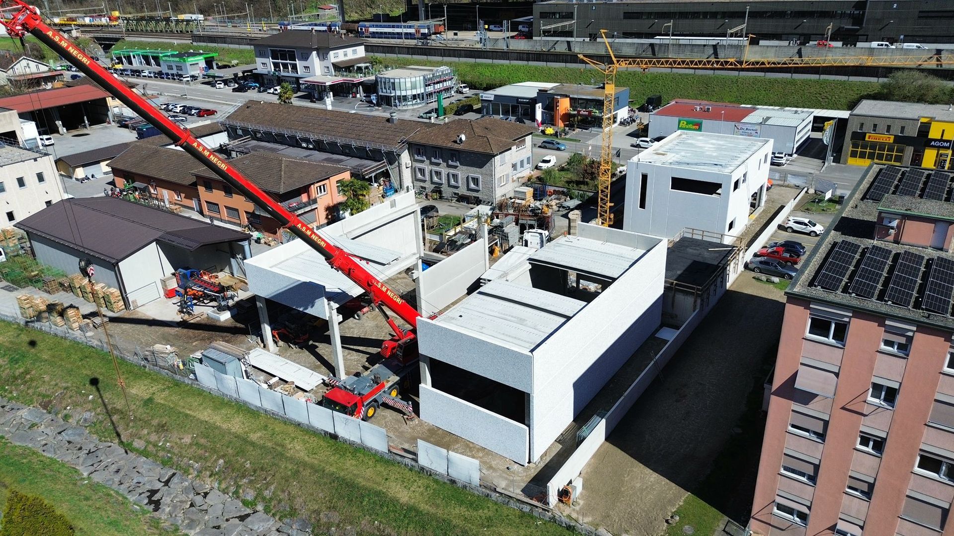 Una vista aerea mostra una gru da costruzione rossa che solleva pannelli per le pareti di un edificio commerciale bianco in un cantiere.
