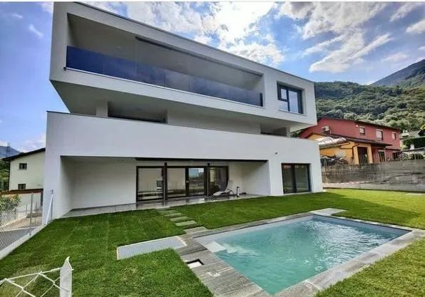 Una moderna casa bianca a due piani con balcone e piscina in giardino, sotto un cielo azzurro con qualche nuvola sparsa.