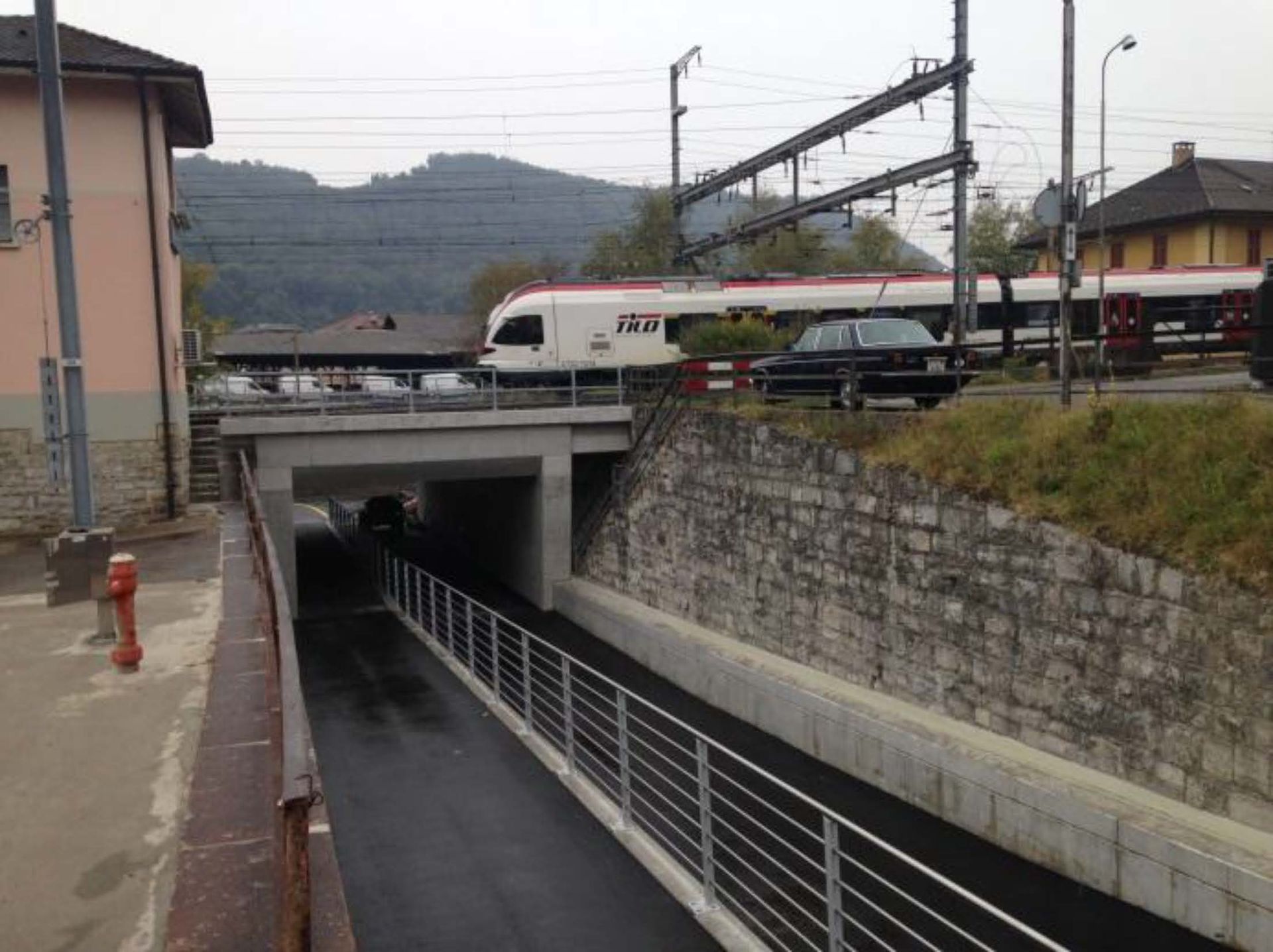 Un treno transita su un sottopassaggio con una ringhiera metallica laterale in una zona suburbana.