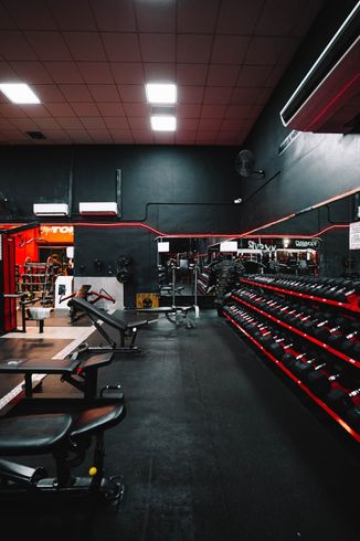 Interior de gimnasio moderno con paredes negras, detalles de LED rojos, bancos de pesas y un estante con mancuernas