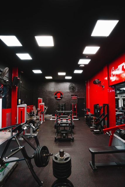El interior de un gimnasio con paredes y techos negros, columnas decorativas rojas, luces cuadradas en el techo