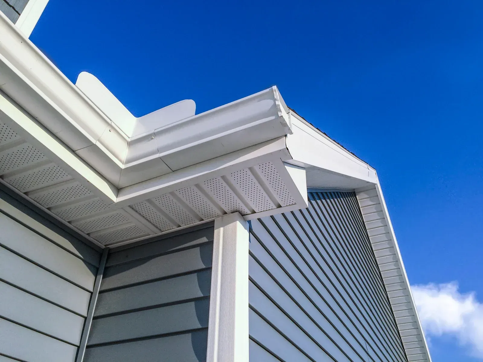 Corner of a house with white trim, gray siding, and blue sky above