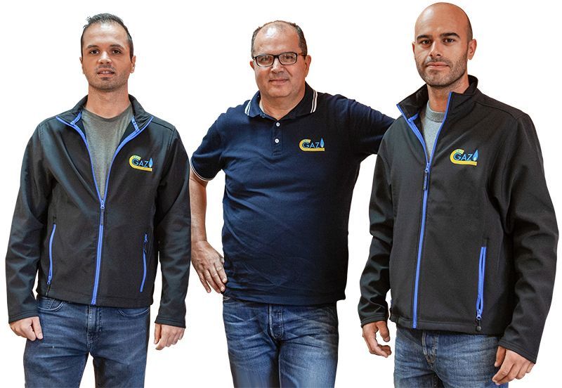 Trois personnes portant des vestes et des chemises aux couleurs de l'entreprise se tiennent côte à côte sur un fond blanc.
