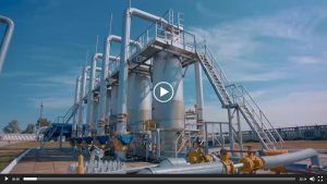 Un complexe industriel avec de grands tuyaux verticaux argentés et des structures métalliques sous un ciel d'un bleu éclatant.