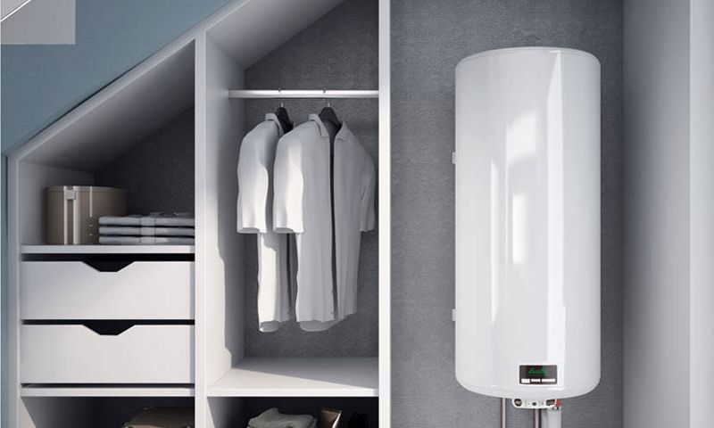 Un chauffe-eau électrique cylindrique blanc, installé dans un placard à côté d'un portant et d'étagères à tiroirs.