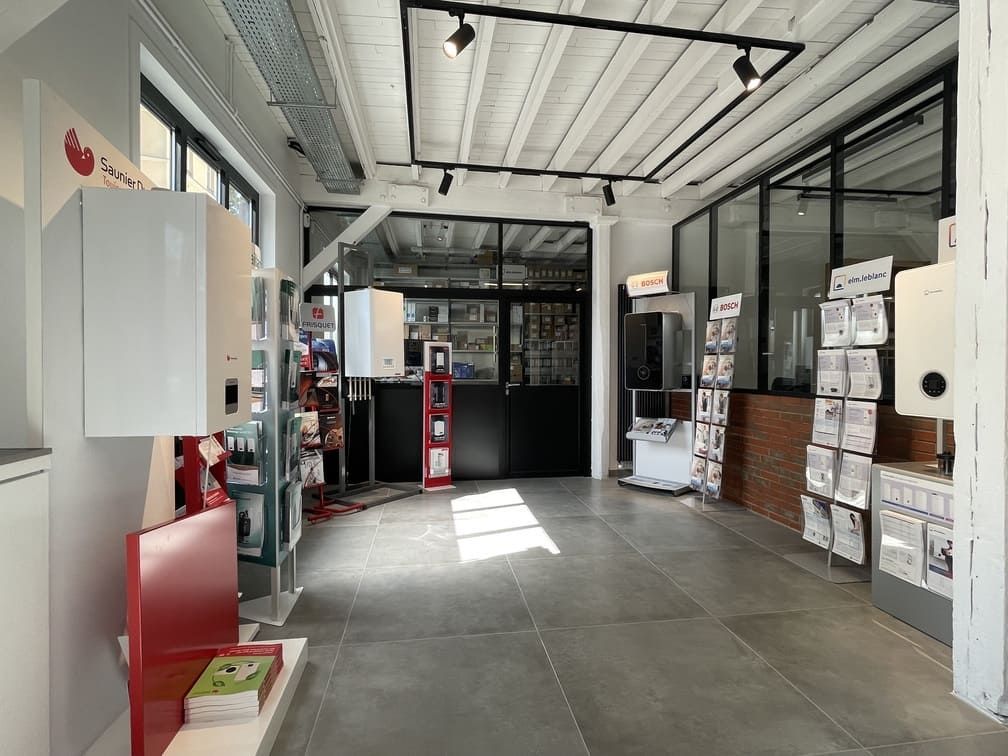 Une salle d'exposition bien éclairée, présentant des chaudières murales blanches, des présentoirs de produits et des brochures d'information sur un sol carrelé.