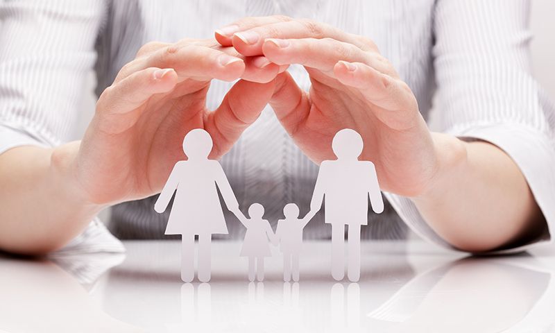 Les mains en coupe protégeaient une silhouette en papier représentant une famille debout sur une surface blanche.