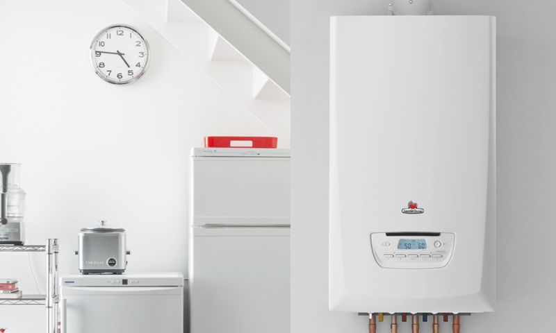 Une chaudière murale blanche dans une cuisine, avec une horloge, un grille-pain et un petit réfrigérateur à proximité.