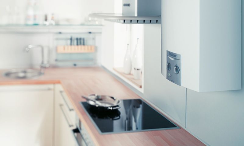 Un élégant plan de travail de cuisine avec une plaque de cuisson moderne et un chauffe-eau blanc mural au-dessus.