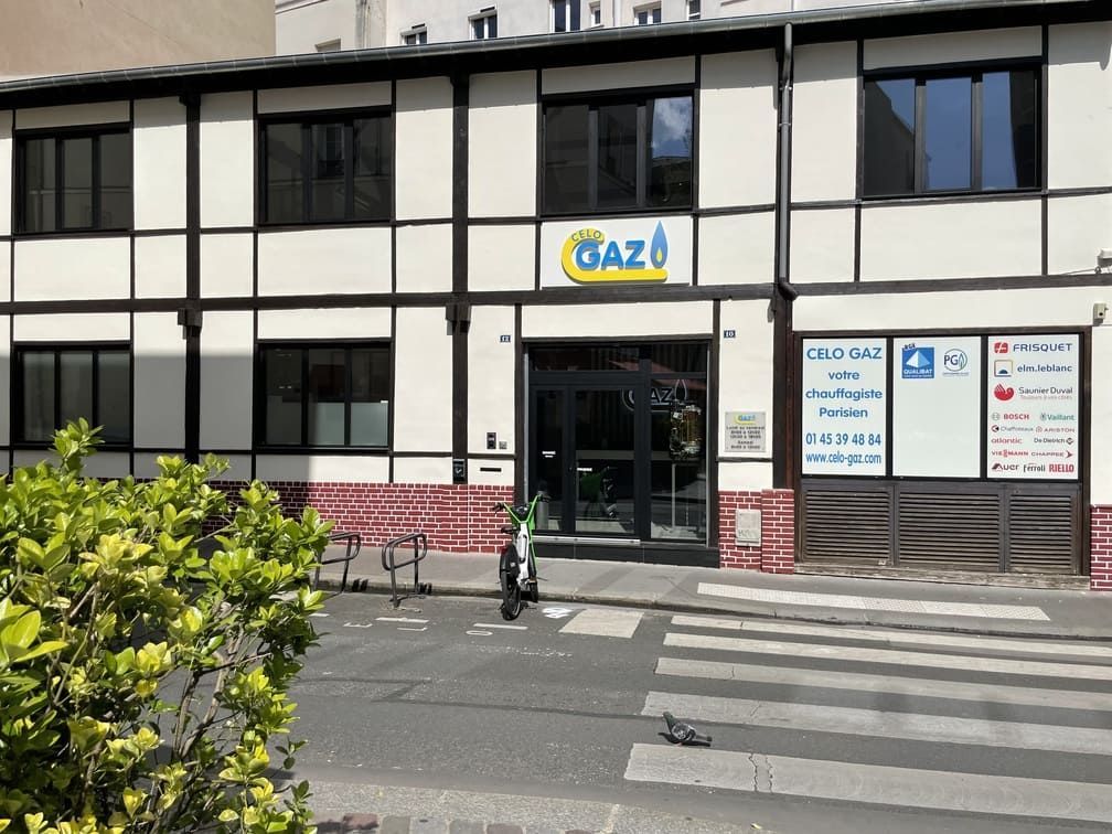 Un bâtiment de deux étages aux murs en stuc blanc, aux poutres en bois sombre et aux fenêtres à cadre noir, orné d'une enseigne centrale GAZ.