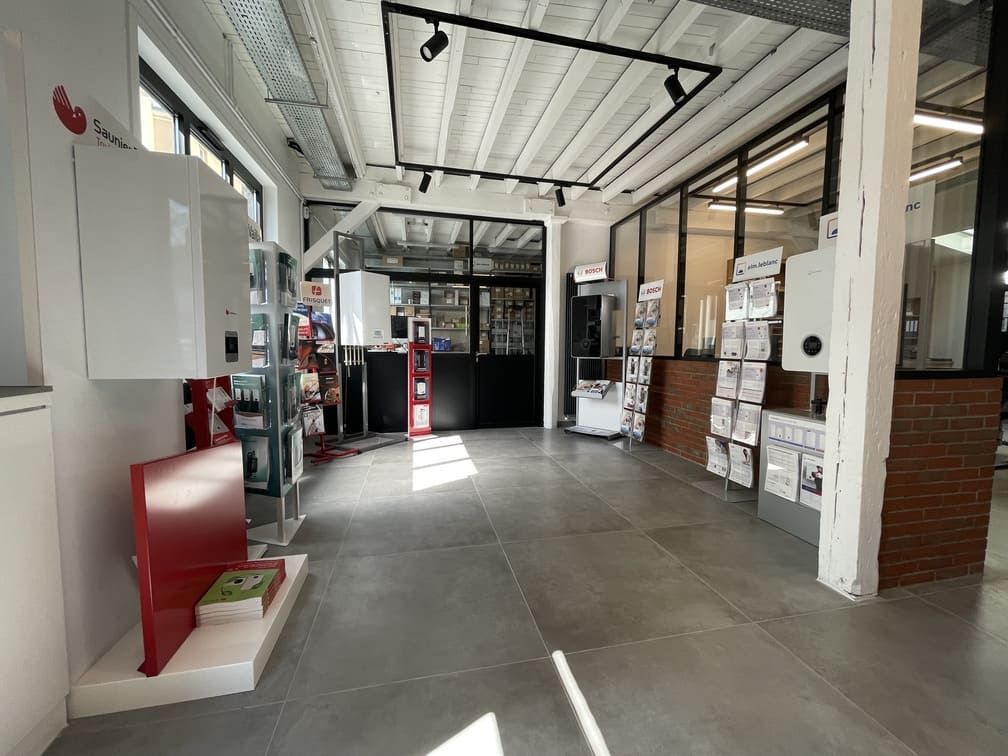 Intérieur de showroom moderne avec sol carrelé, présentoirs de chaudières et présentoirs à brochures sous un plafond industriel éclairé.