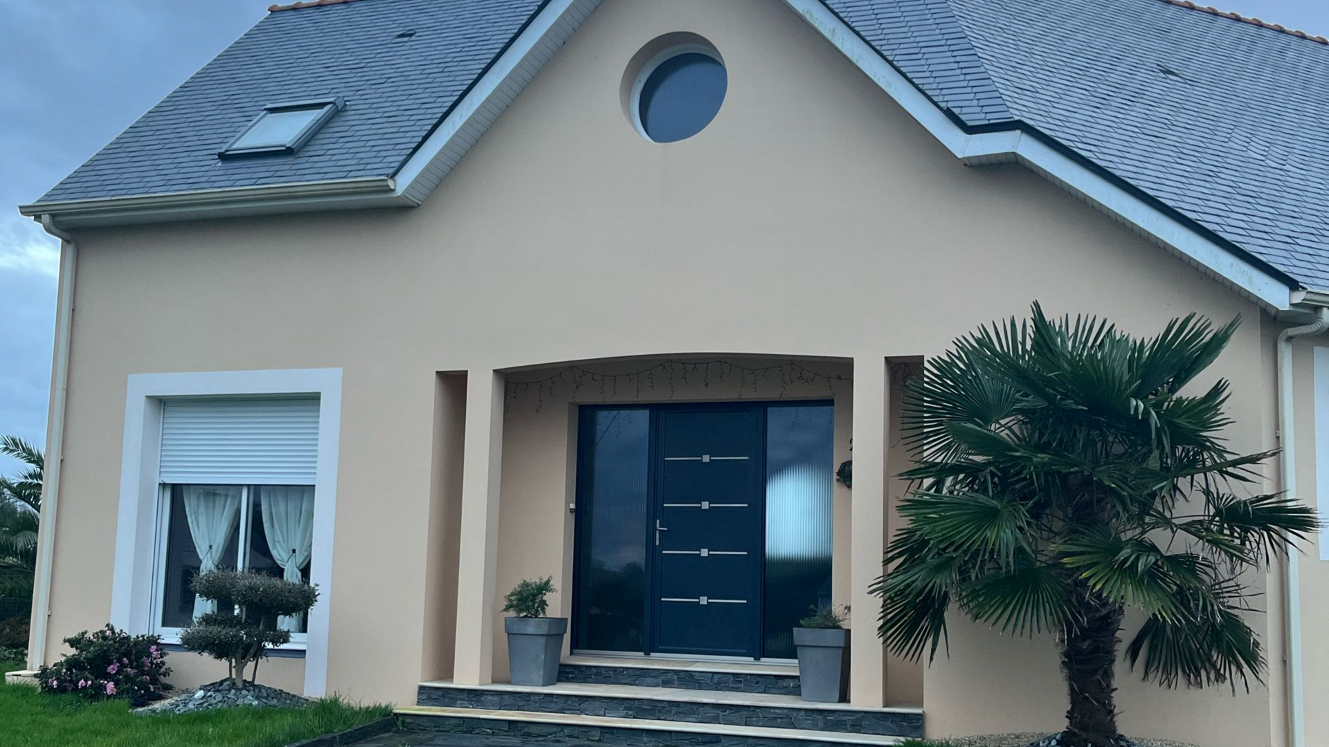 Une personne peint une corniche blanche au pinceau, en extérieur. Le mur au-dessus est texturé et beige.