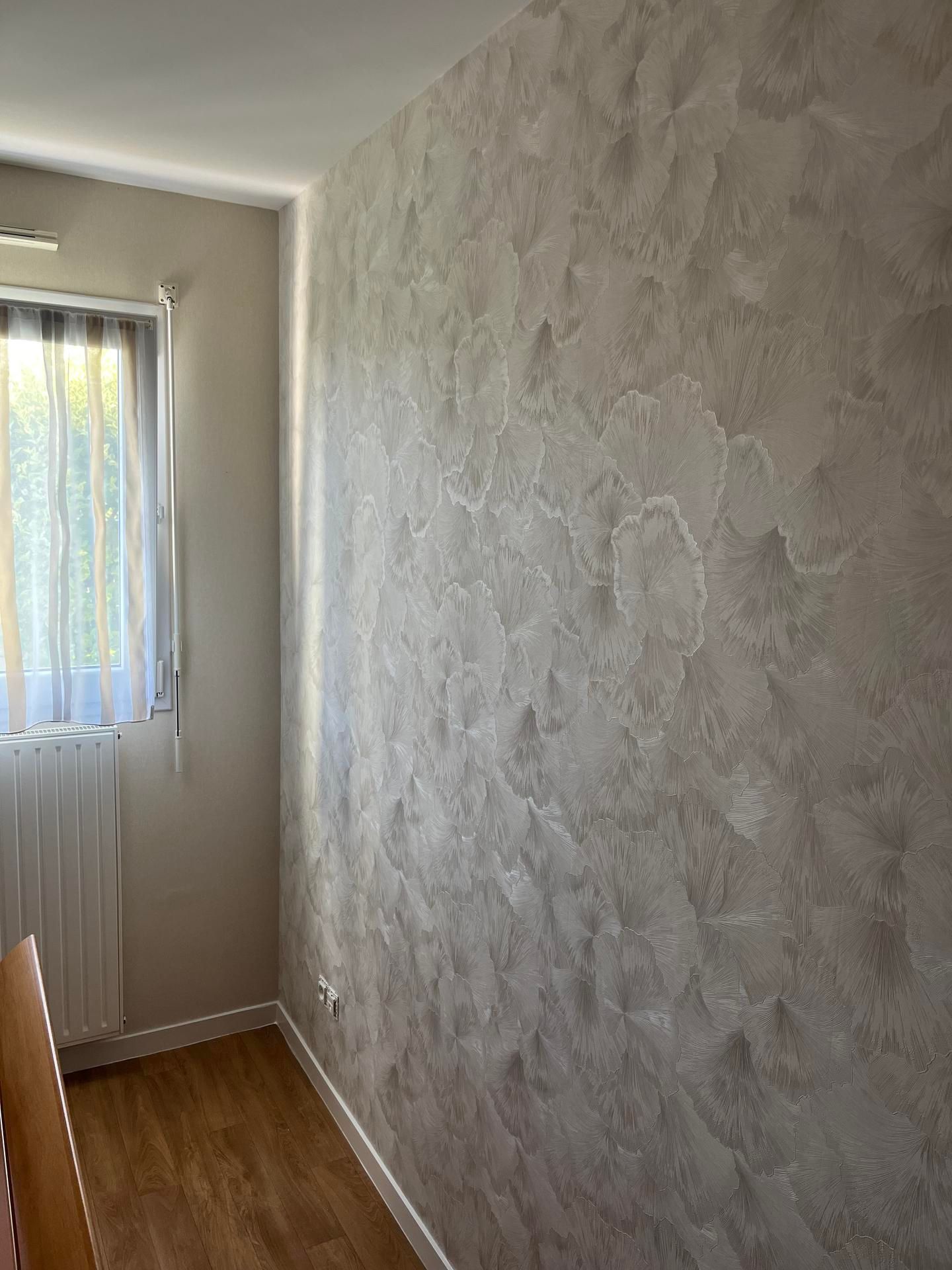 Intérieur de la pièce avec mur gris texturé. Fenêtre avec voilage à gauche. Parquet.