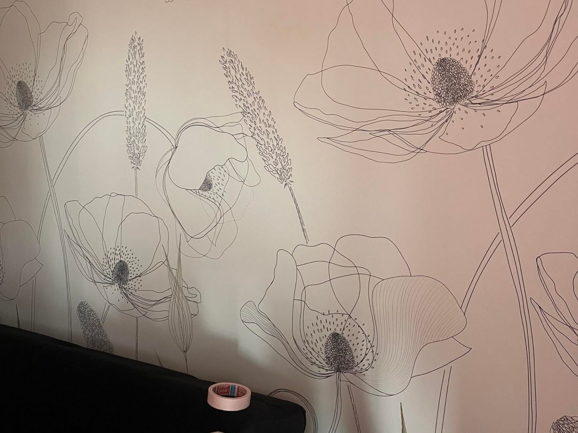 Papier peint à motifs floraux avec des contours noirs et un rouleau de ruban adhésif sur une surface noire.