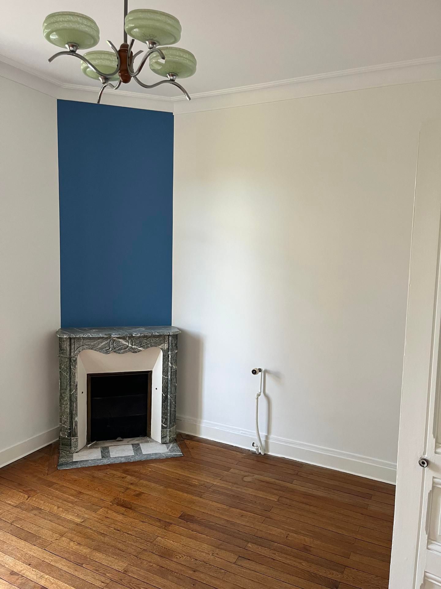 Pièce vide avec cheminée, mur d'accent bleu, plancher de bois franc, lustre et murs blancs.
