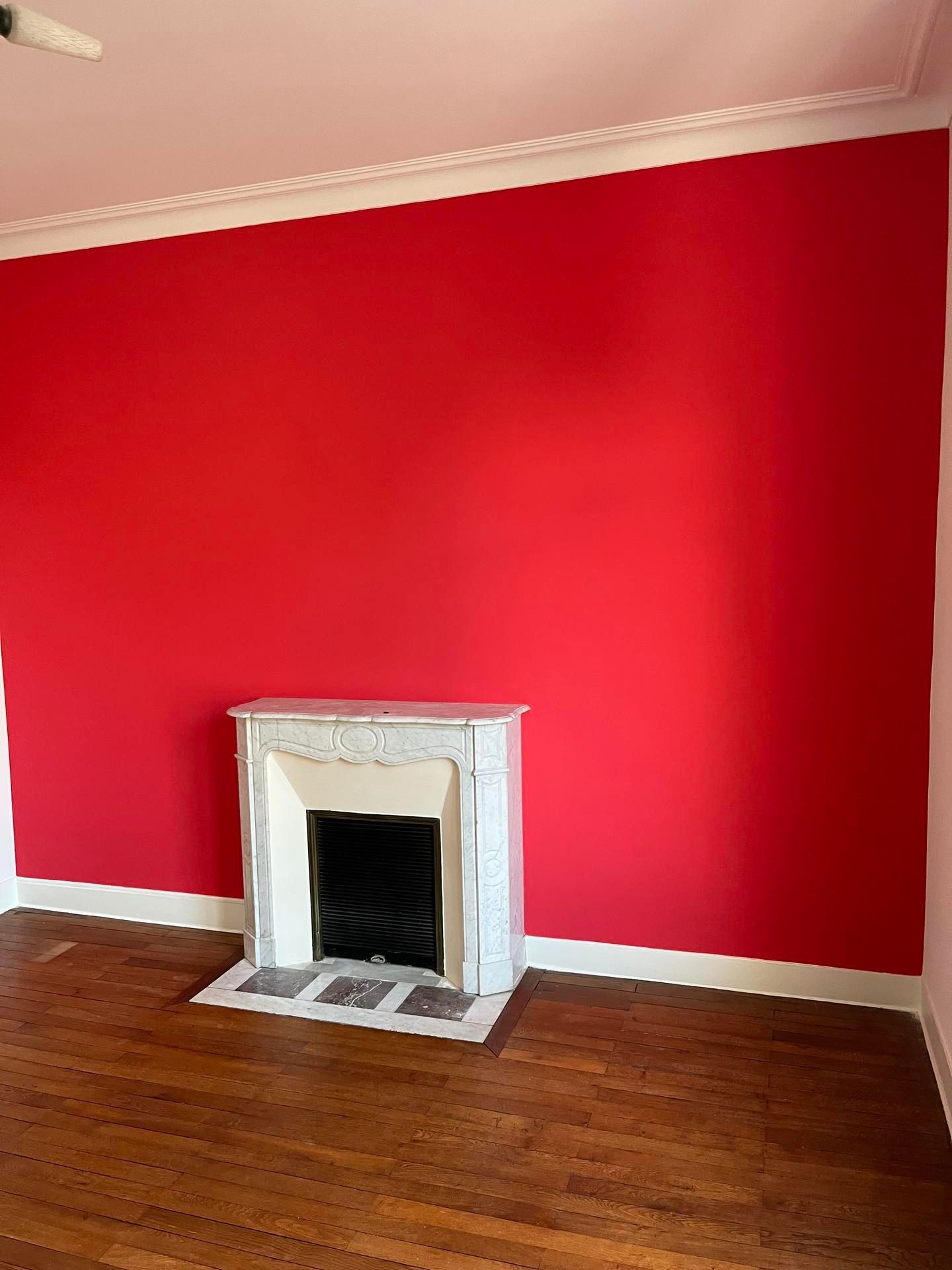 Mur rouge avec une cheminée blanche et un plancher en bois foncé.