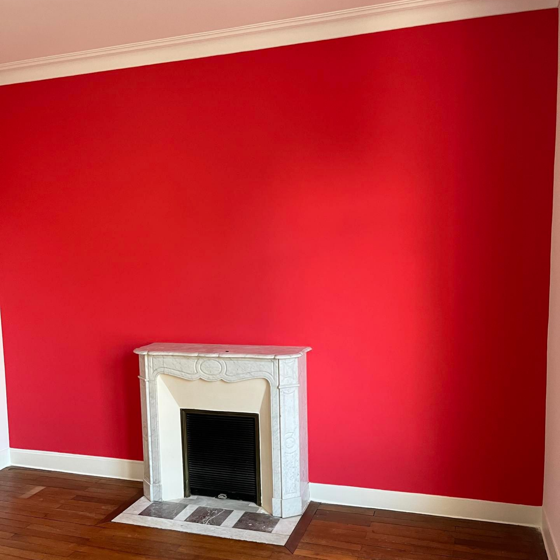 Mur rouge avec cheminée et moulures blanches et parquet.