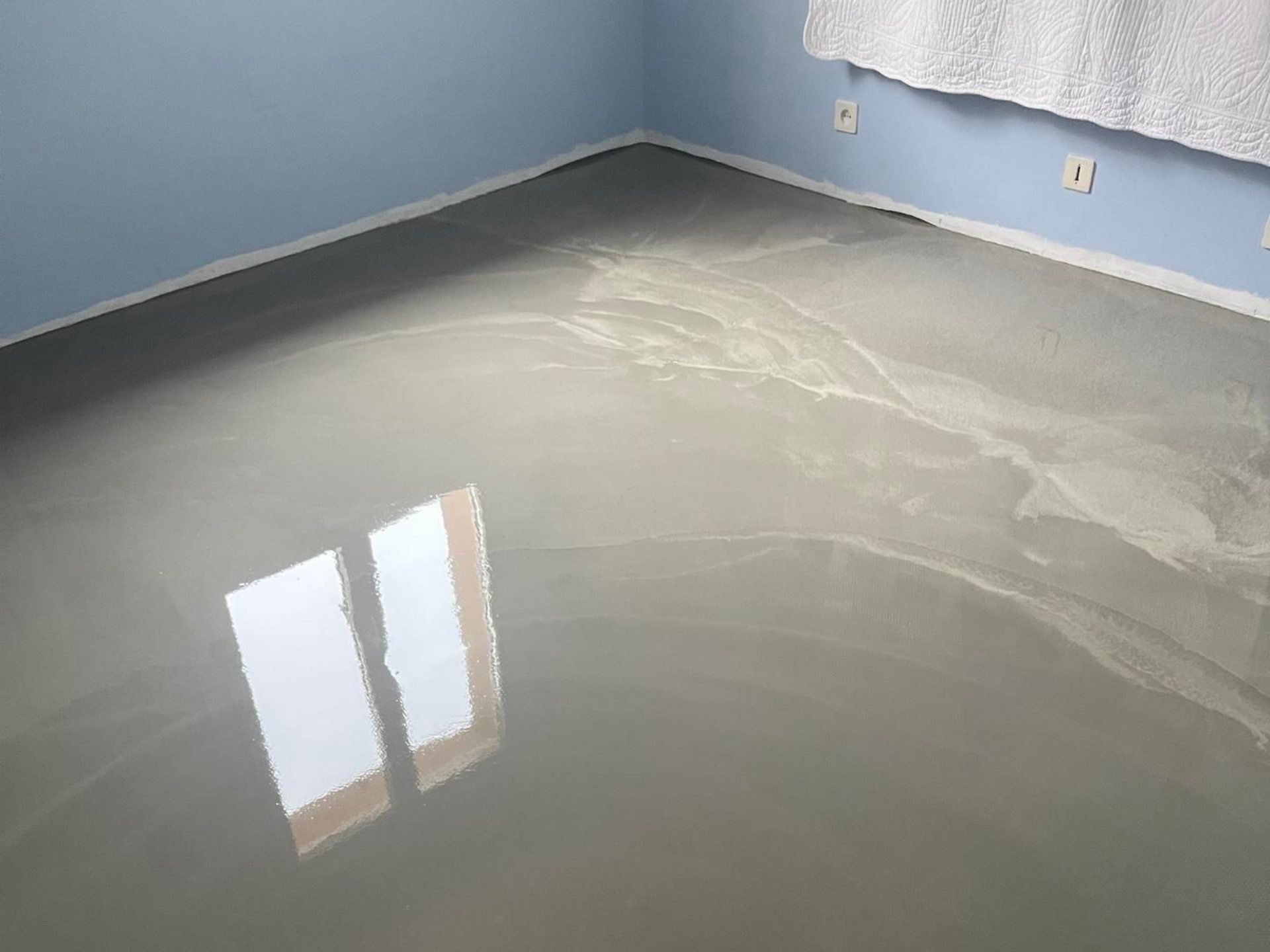 Sol époxy gris brillant réfléchissant la lumière d'une fenêtre dans une pièce aux murs bleus.