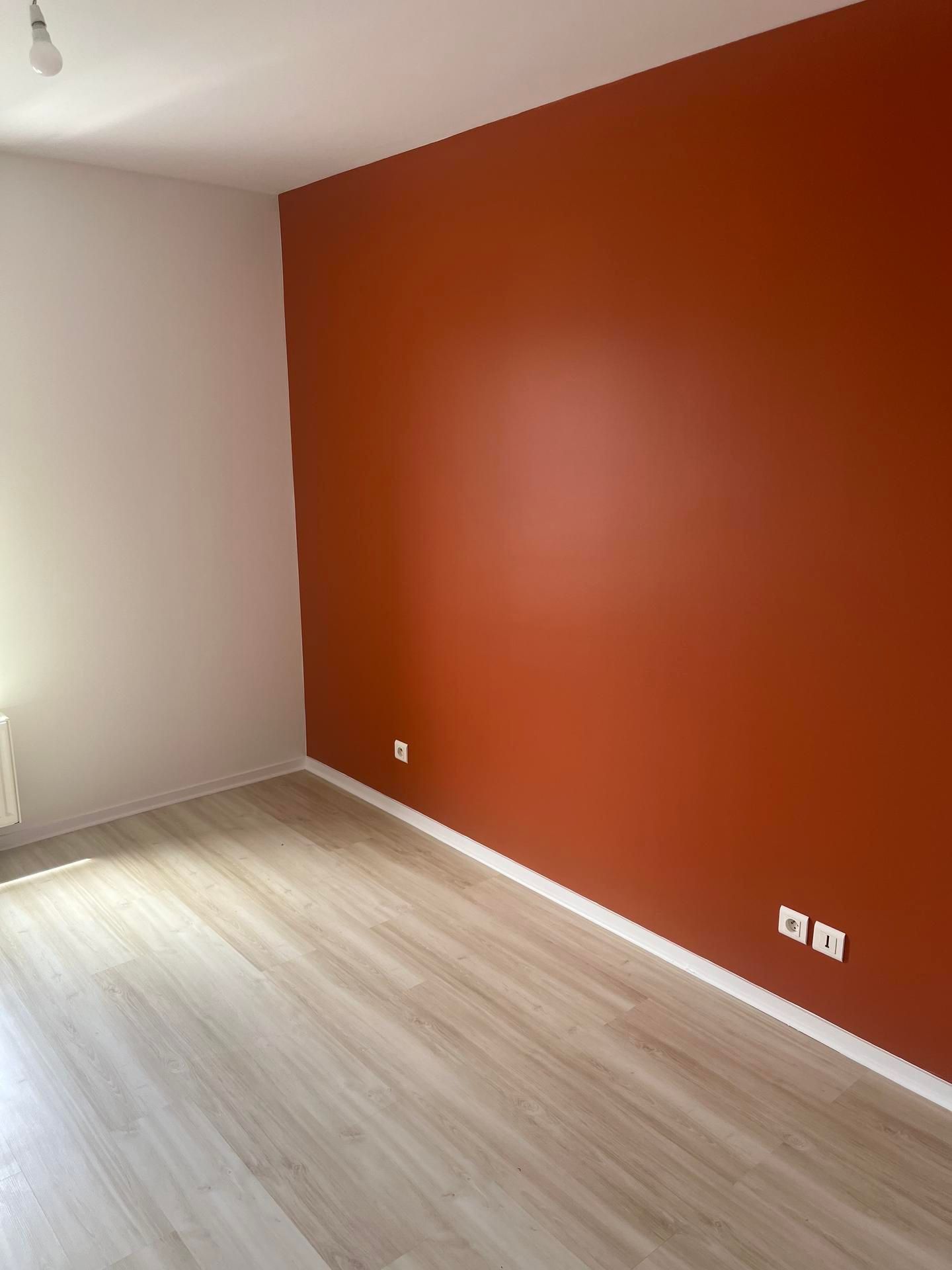 Chambre avec parquet en bois clair, murs blancs et rouge orangé.