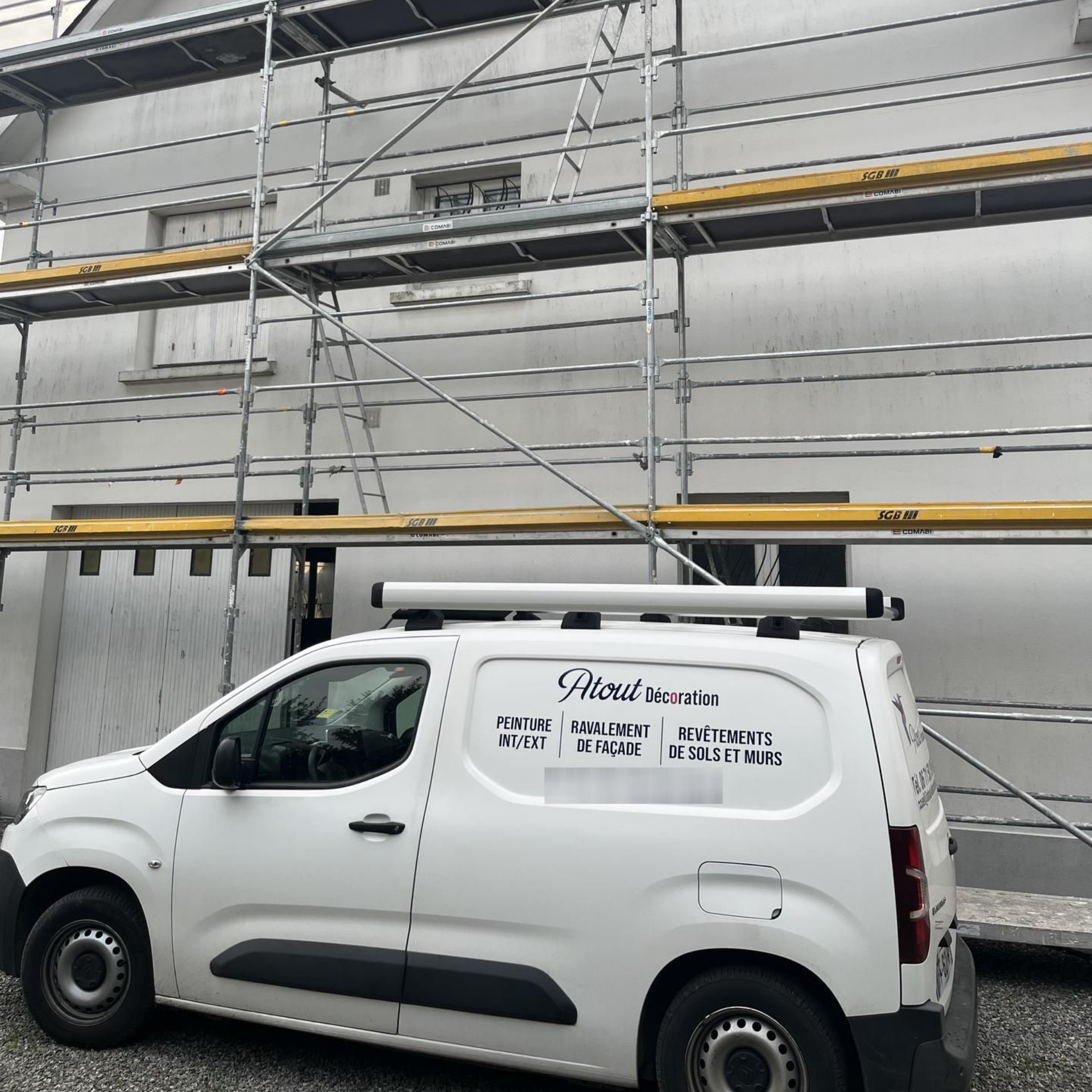 Camionnette blanche avec le logo de l'entreprise garée près d'un bâtiment avec des échafaudages.
