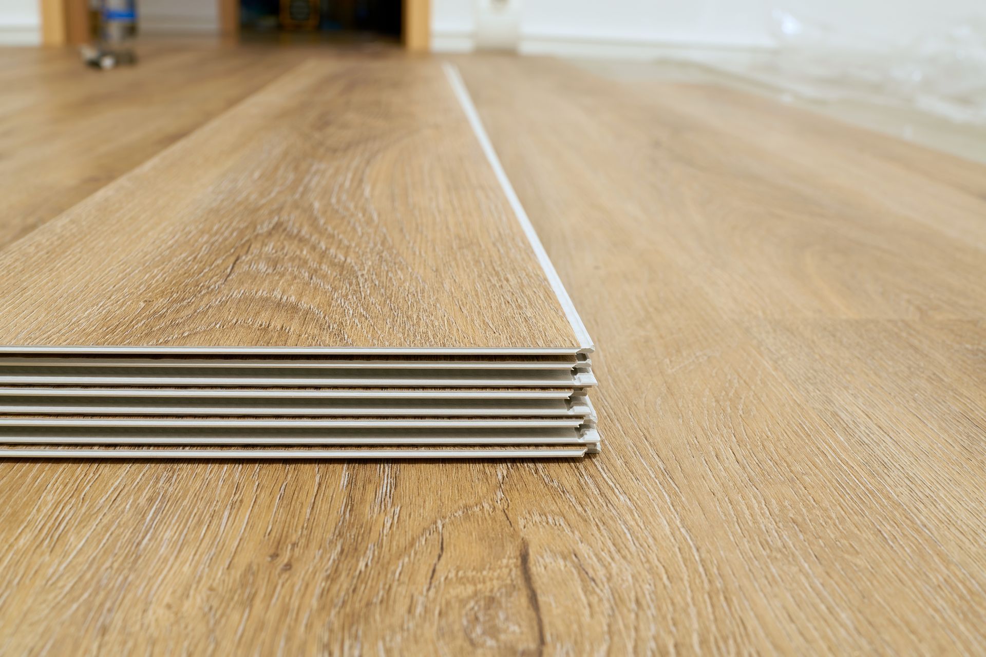 Pile de planches de parquet aspect bois brun clair prêtes à être installées sur le revêtement de sol existant.
