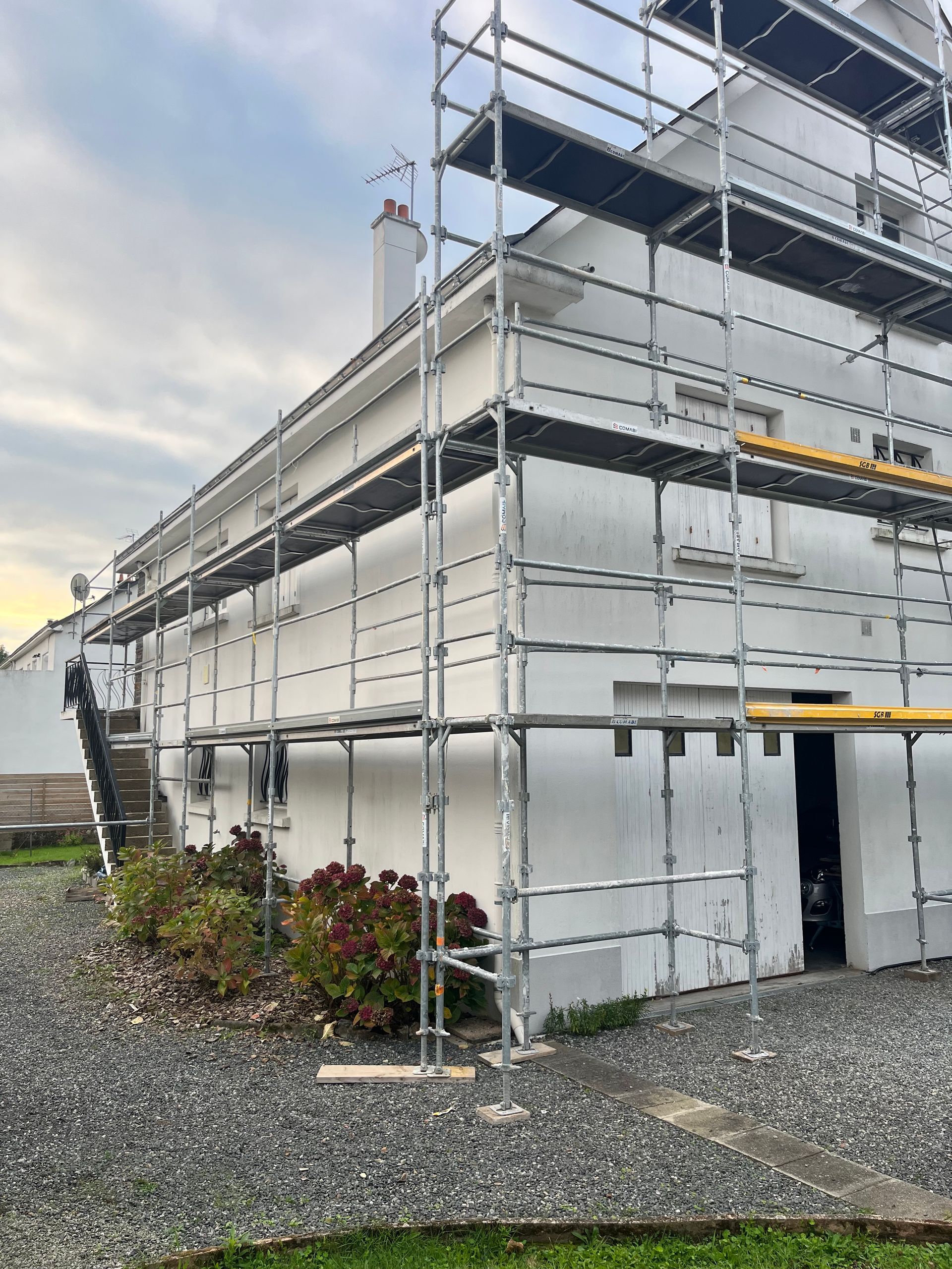 Application manuelle d'une teinture brun rougeâtre sur des planches avec un pinceau, près d'une charnière métallique.