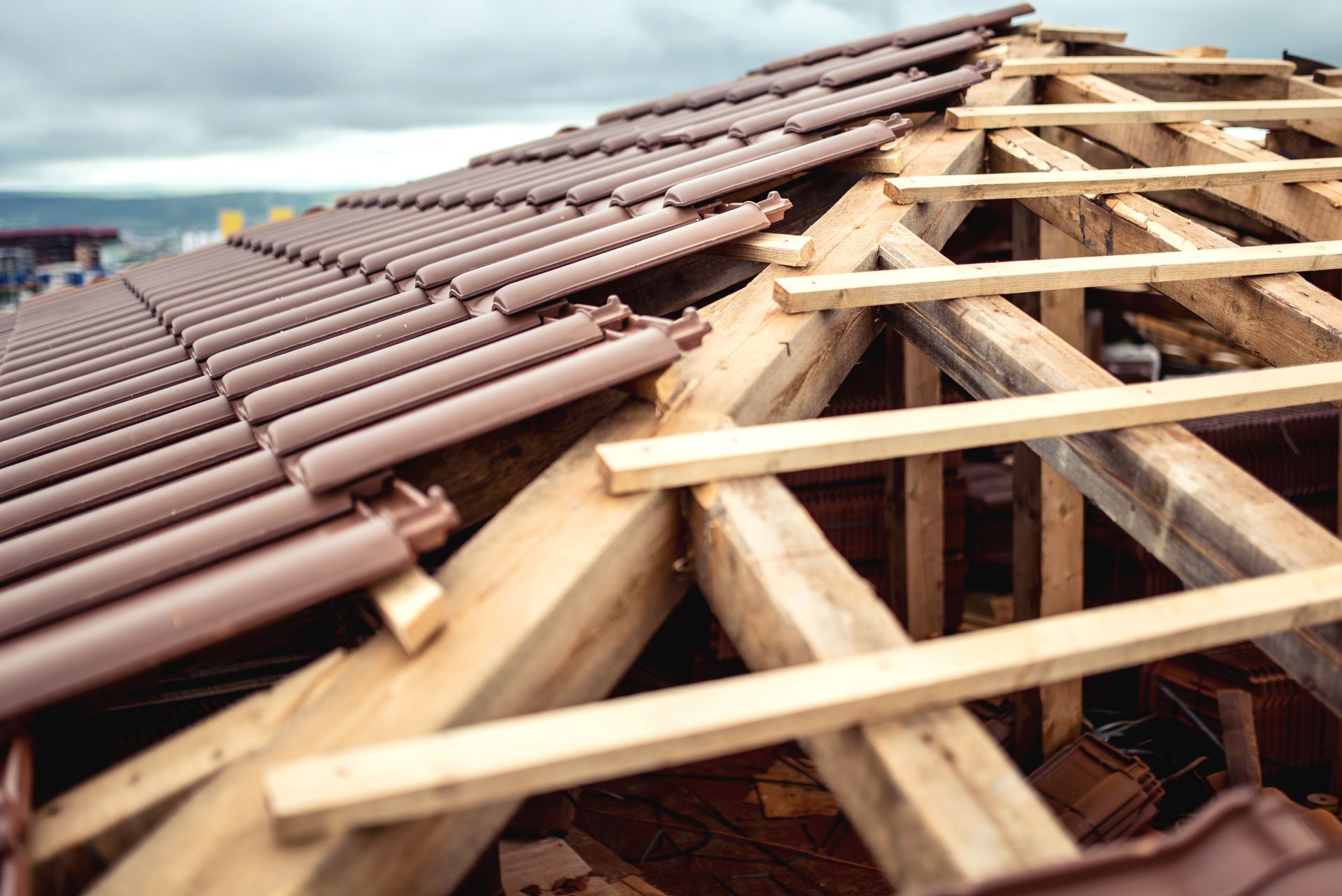 Toiture en construction, pose de tuiles brunes sur des chevrons en bois sous un ciel nuageux.