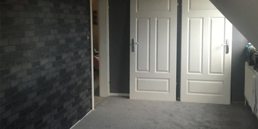 Zimmer mit zwei weißen Türen, grauem Teppichboden und einer dunklen Backsteinwand.