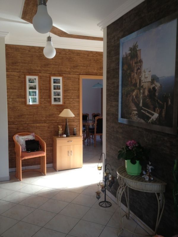 Flur mit Fliesenboden, strukturierten braunen Wänden, Kunstwerken, einem Stuhl und einem Tisch mit Pflanzen.