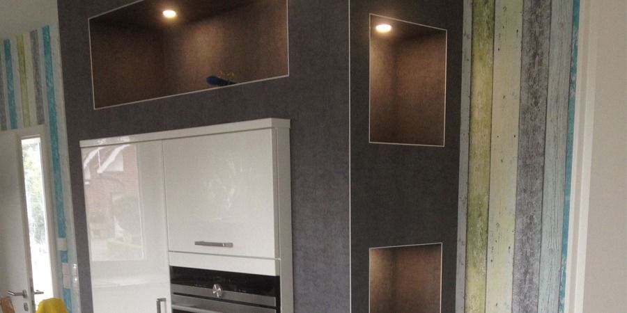 Einbauschränke und Regale mit Beleuchtung in einer Küche mit Wandverkleidung in Holzoptik.