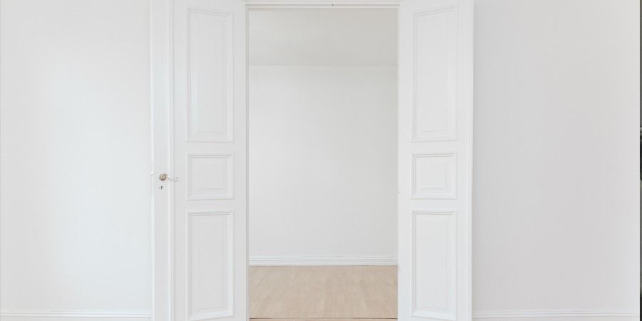 Weiße Doppeltüren öffnen sich zu einem hellen Raum mit hellen Holzböden.