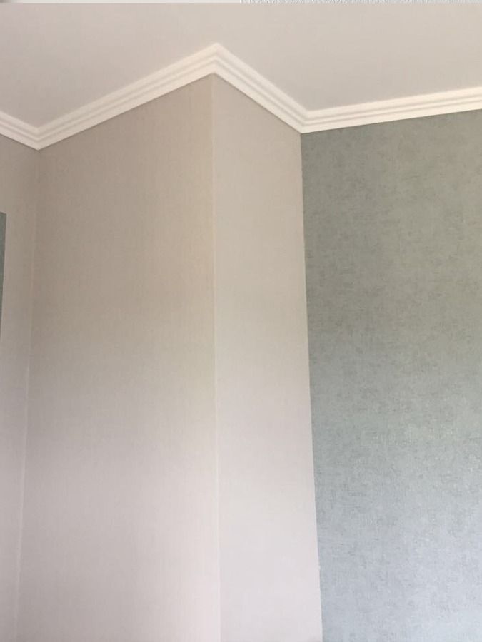 Zimmerecke mit weißer Zierleiste und beigen und grünen Wänden.